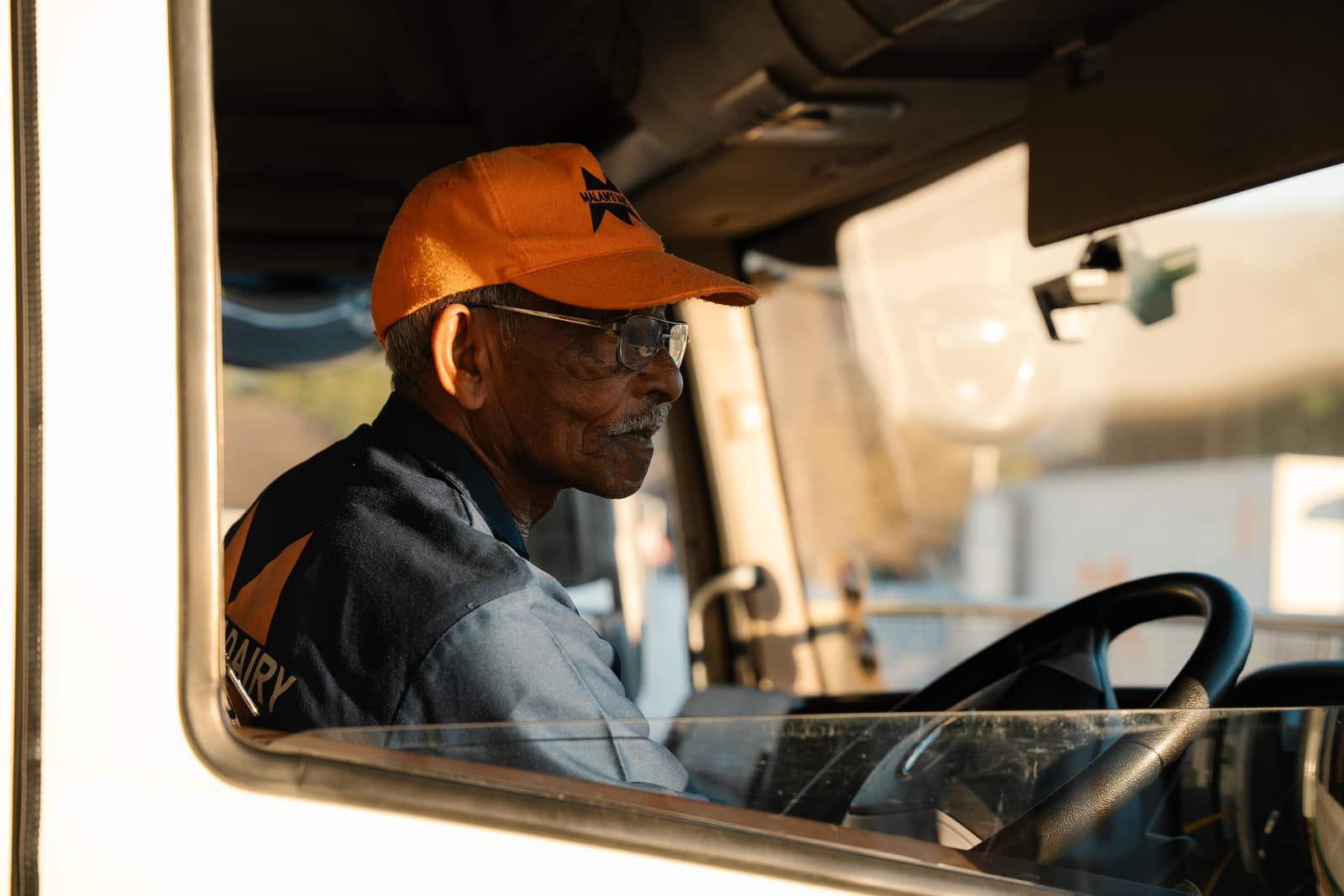 A Malan's Dairy driver in a branded cap at the wheel in golden light