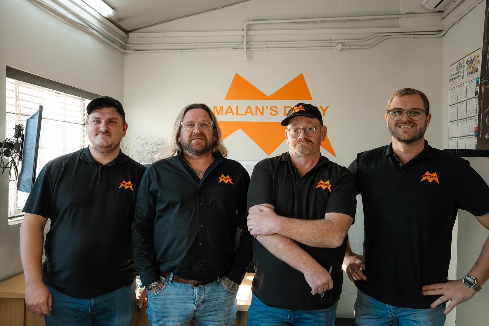 The Malan's Dairy management team by the branded office wall