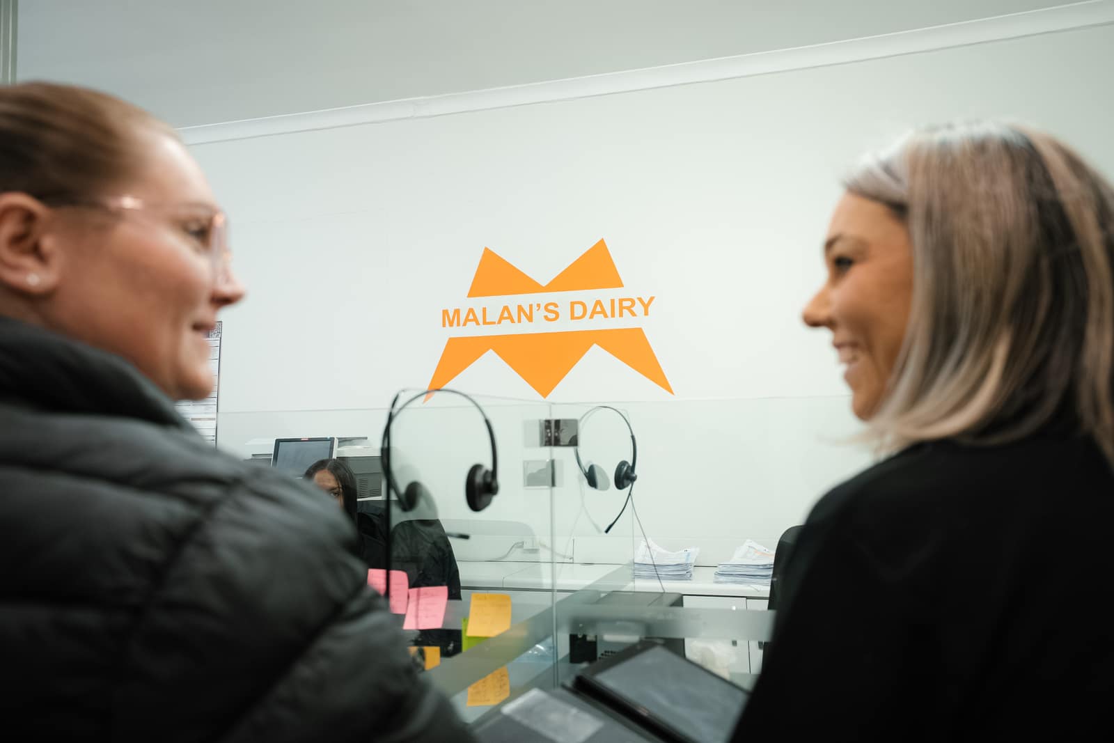 Two Malan's Dairy office colleagues sharing a laugh by the branded wall