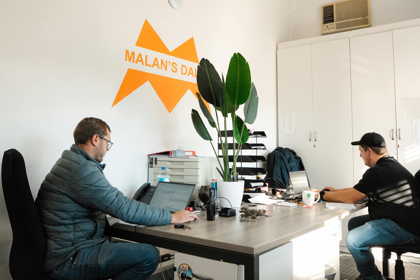 Two Malan's Dairy managers working at their desks under the branded wall