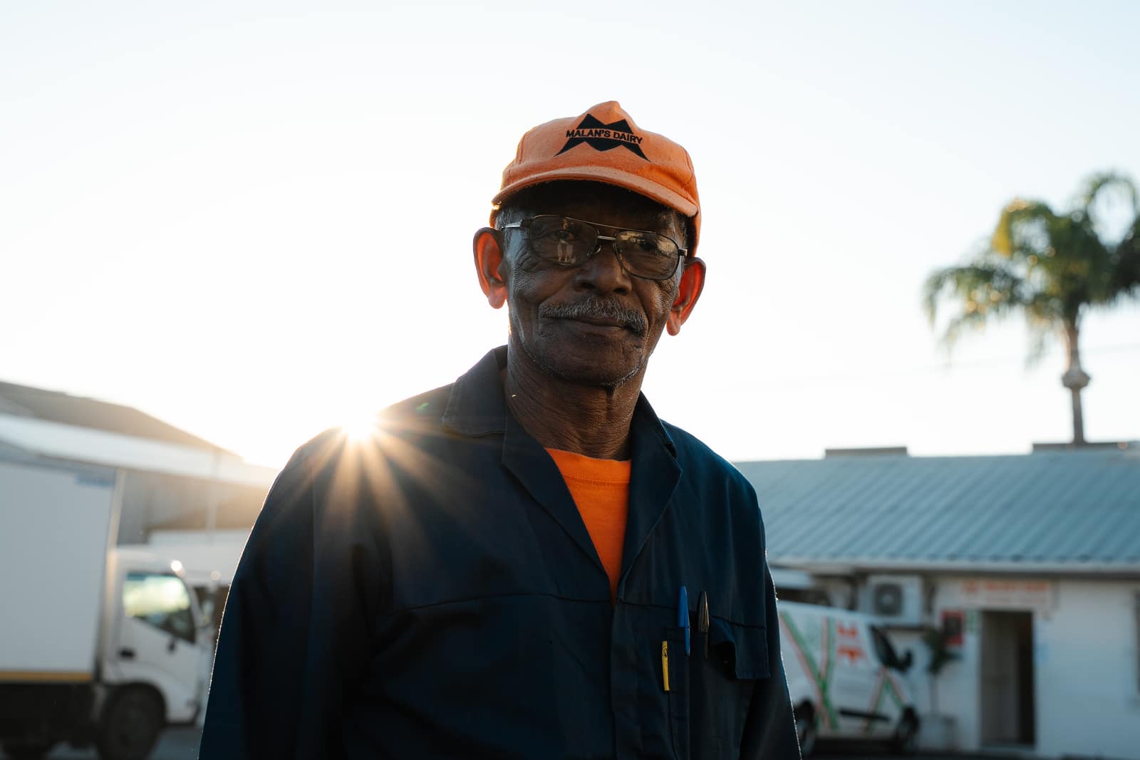 A veteran Malan's Dairy yard worker in a branded orange cap at sunset